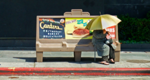 Women sitting under the shade of an umbrella at a bus stop in full sun